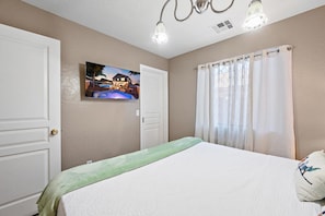A bedroom with a bed, a painting, a window with curtains, and a ceiling light fixture.