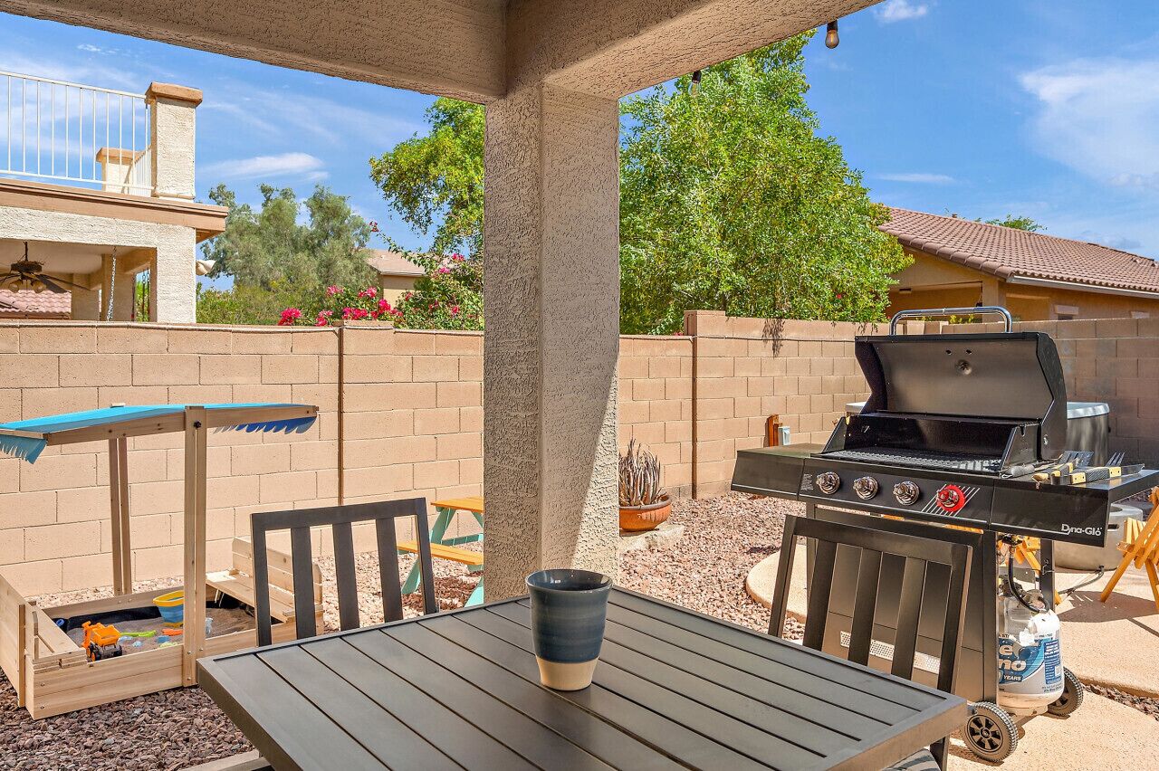 An outdoor patio with a grill, a table, and a play area.