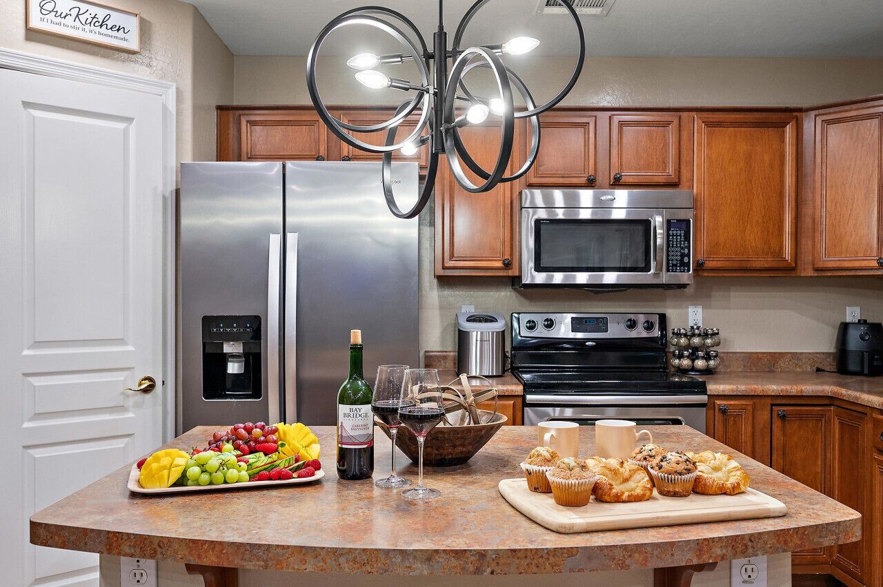 A kitchen with stainless steel appliances, wooden cabinets, a granite countertop, and a chandelier.