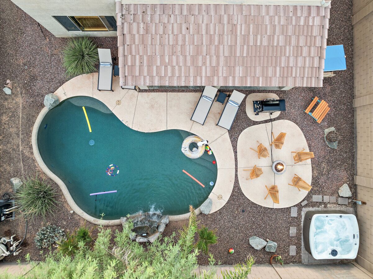A swimming pool with a hot tub, lounge chairs, and a fire pit area.
