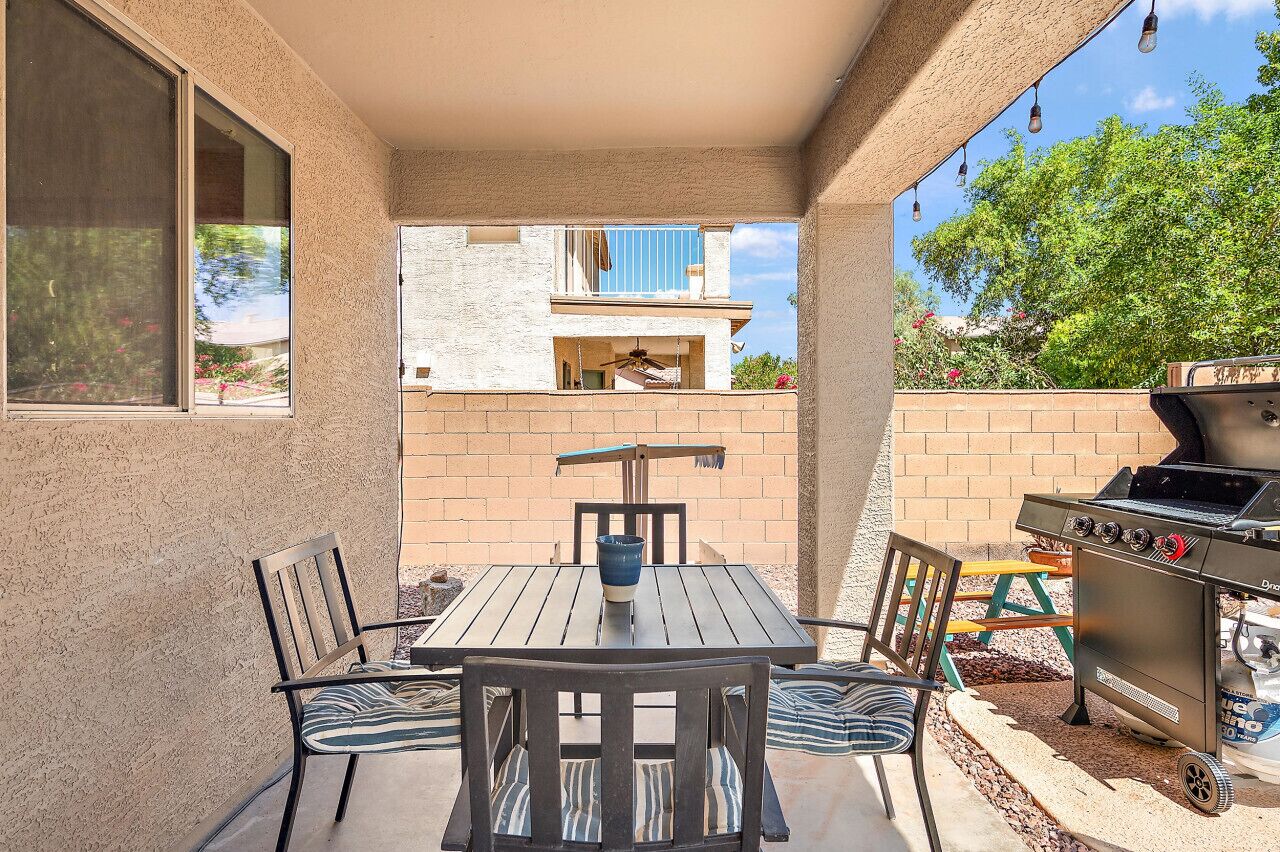 An outdoor patio with a table and chairs, a grill, and a view of a building with balconies.