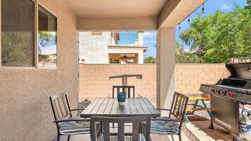 An outdoor patio with a table and chairs, a grill, and a view of a building with balconies.