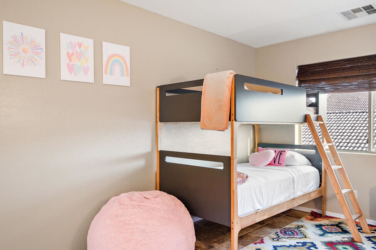 A bunk bed with a ladder, a pink bean bag, and three wall art pieces.