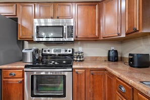 A kitchen with wooden cabinets, a stainless steel stove, a microwave, a toaster, and a coffee maker. - Desert Oasis Amazing Pool/Waterfall/Firepit/Office (Casa Grande)