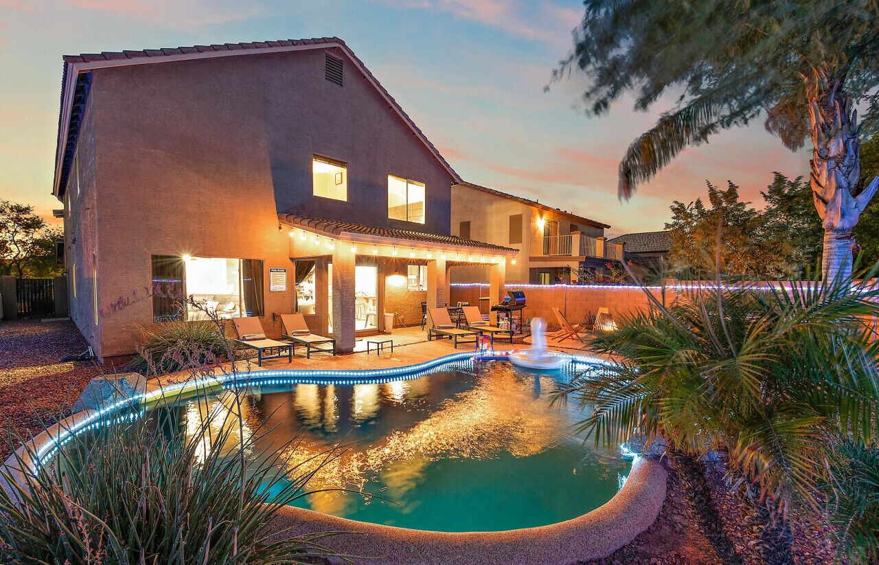 A two-story house with a swimming pool, outdoor seating, and a well-lit patio area.