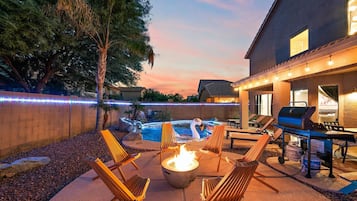 Une terrasse extérieure dotée d’un foyer, de chaises longues, d’un barbecue et d’une piscine.