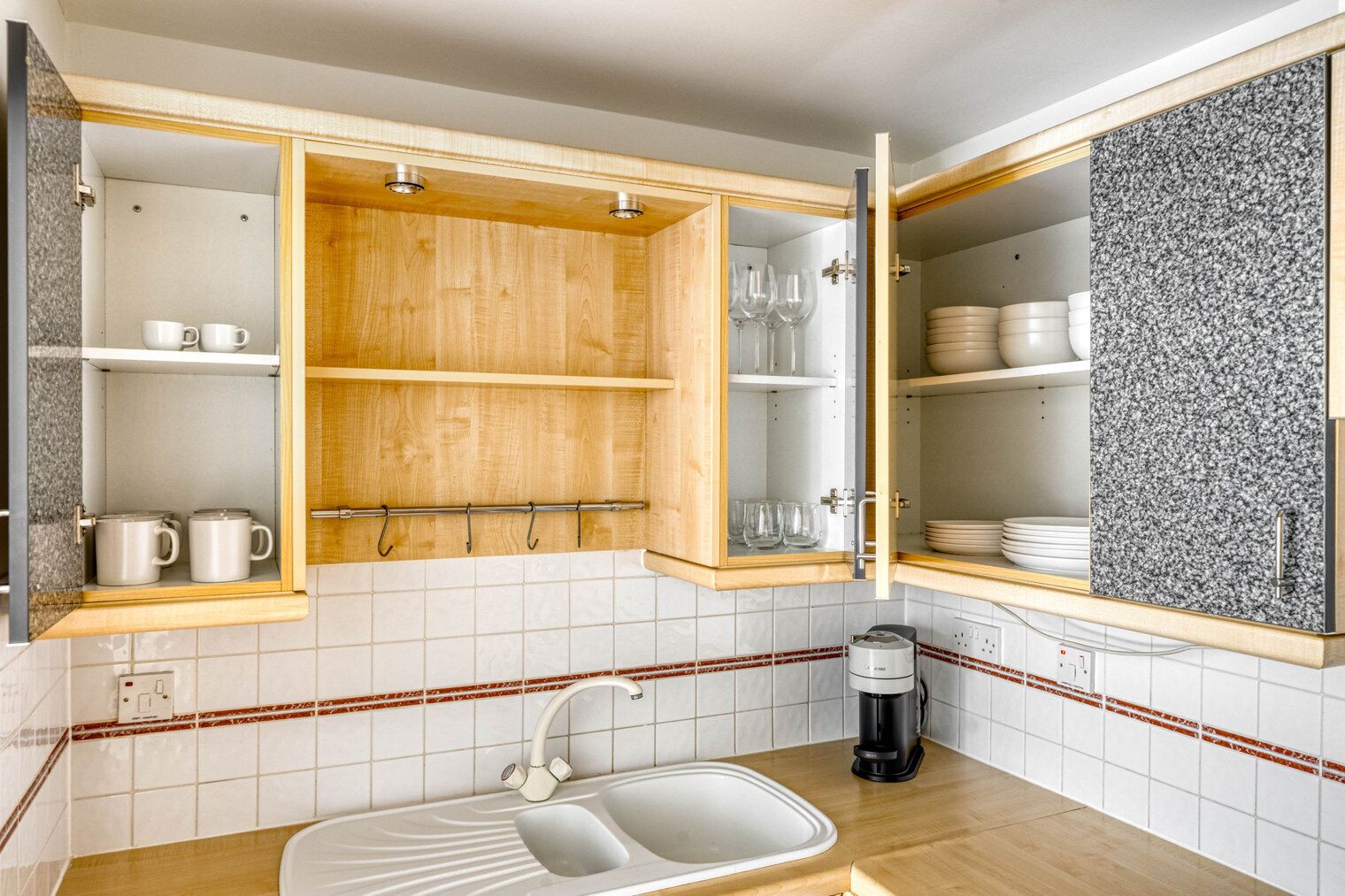 A kitchen with a sink, a coffee maker, and open cabinets with dishes and glasses.