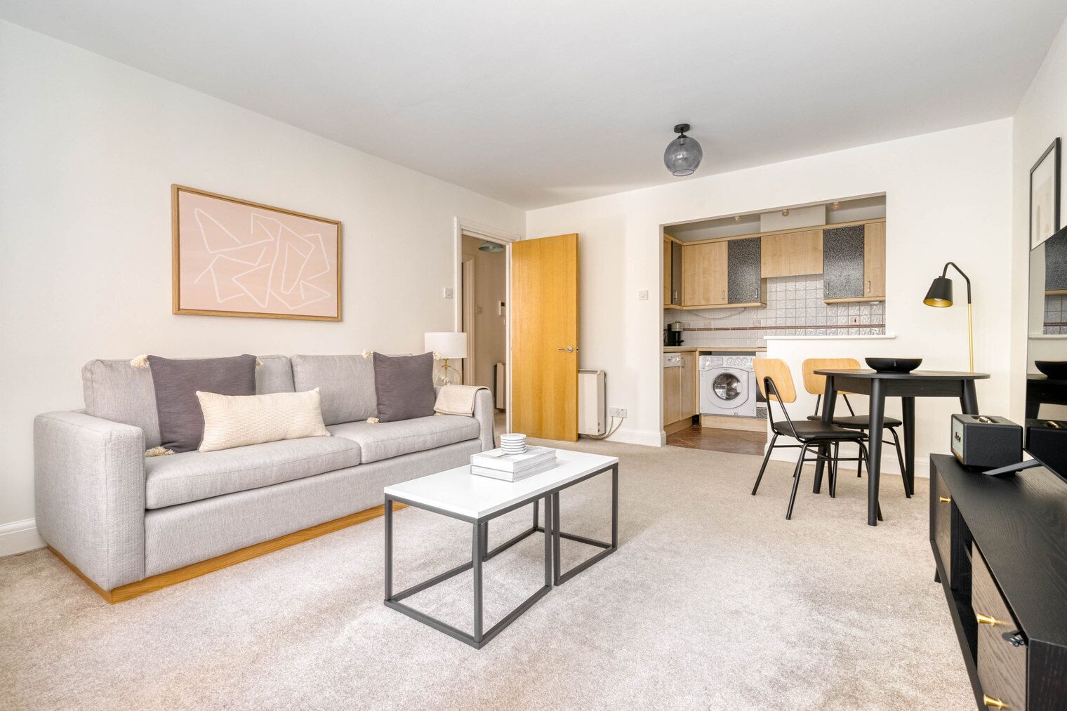 Ein modernes Wohnzimmer mit einem grauen Sofa, einem Couchtisch und einer Küche im Hintergrund.