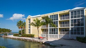 A hotel with a waterfront view, featuring a pool, palm trees, and a red lounge chair.
