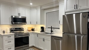 A modern kitchen with white cabinetry, stainless steel appliances, and a wooden floor. - City Center Modern Apartment (Charlottetown)