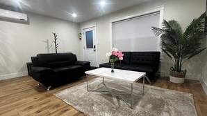 A living room with a black sofa, a white coffee table, a fluffy rug, and a potted plant. - City Center Modern Apartment (Charlottetown)