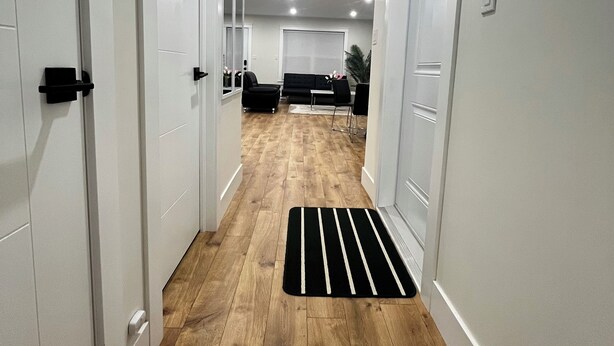 A hallway with wooden flooring, white doors, and a black and white striped mat. - City Center Modern Apartment (Charlottetown)