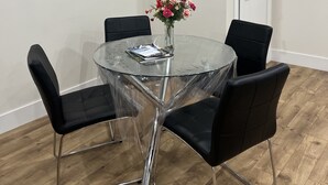 A round glass table with four black chairs, a vase with flowers, and a framed picture on the wall. - City Center Modern Apartment (Charlottetown)