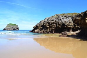 A beach with a rocky cliff and a small island.