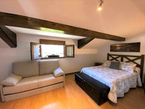 A bedroom with a bed, a sofa, a window, and wooden beams on the ceiling.