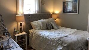 A bedroom with a bed, two bedside lamps, a nightstand, a window with curtains, and a painting on the wall. - RENTAL - 4.7 miles away, newly remodeled ranch home (Oshkosh)