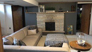 A living room with a stone fireplace, a sofa, a coffee table, and a small round table with a glass bowl. - RENTAL - 4.7 miles away, newly remodeled ranch home (Oshkosh)