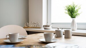 Ein Esstisch mit weißen Tassen und Untertellern, eine weiße Vase mit Grünpflanzen und ein dekoratives Metallschild.