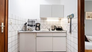Eine kleine Küche mit weißen Schränken, einer Arbeitsplatte und verschiedenen Geräten, darunter eine Kaffeemaschine und ein Wasserkocher.