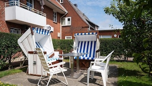 Eine Terrasse im Freien mit einem Tisch und zwei Stühlen, einer davon mit einem blau-weiß gestreiften Kissen.