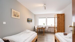 Ein Zimmer mit zwei Einzelbetten, einem Schreibtisch mit Stuhl, einem Fenster und einem Holzschrank.