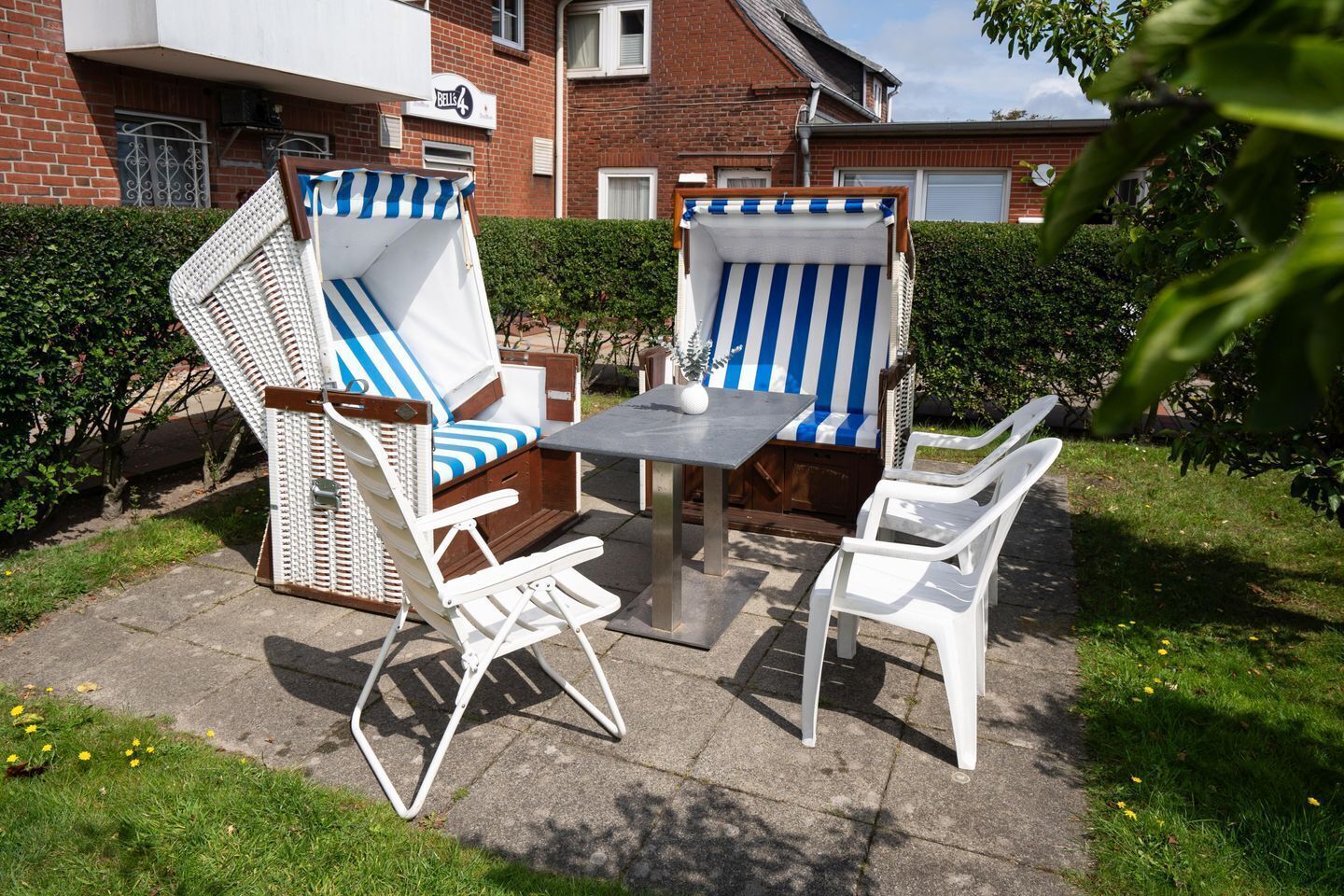 Un patio exterior con dos sillones a rayas, una mesa y una lámpara de mesa blanca pequeña.