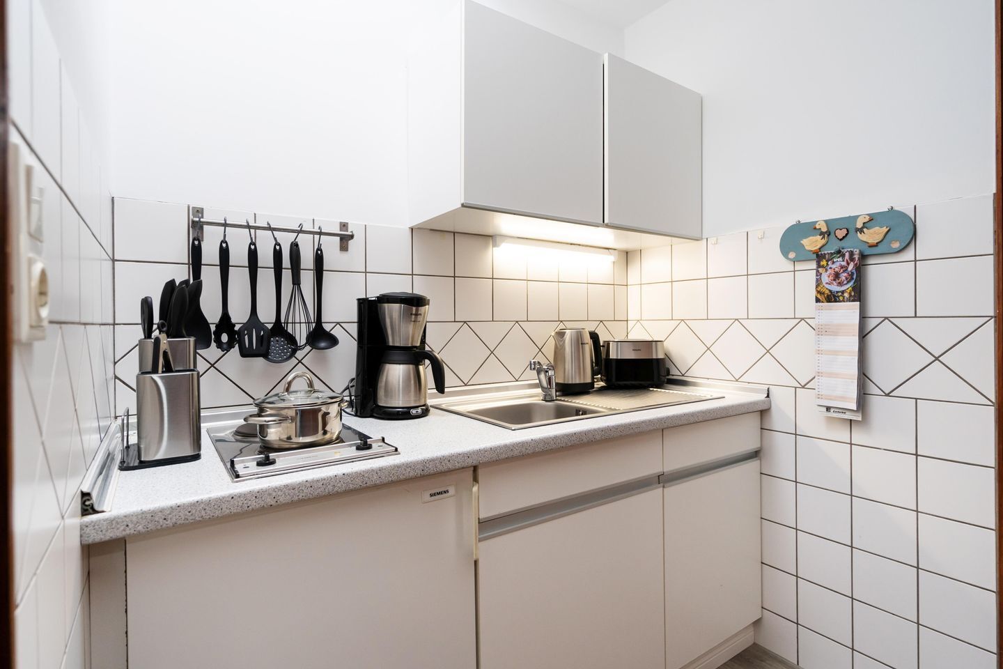 A modern kitchen with white cabinets, a stainless steel coffee maker, a kettle, and a toaster.