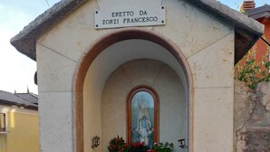 Un petit sanctuaire avec une statue, une inscription indiquant « Érigé par Zorzi Francesco », et des plantes en pot.