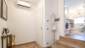 Un couloir avec une porte blanche, une petite table sur laquelle est posé un vase décoratif et des toilettes dorées.
