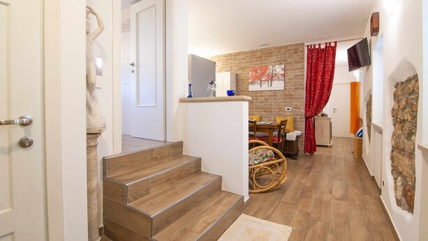 Un escalier menant à une salle à manger avec un mur en briques, un téléviseur et un rideau rouge.