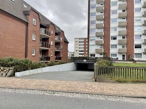 Kerrostalo, jossa on useita kerroksia, parvekkeet ja pysäköintialue sen edessä.