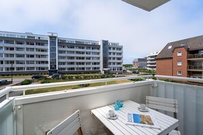 A balcony with a table, chairs, and a book. In the background, there are multi-story buildings and a road with cars. - Sylter Residenz - Modern apartment near the beach, with a balcony, parking space, and Wi-Fi. (Sylt)