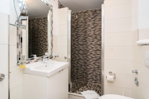 A modern bathroom with a white sink, a mirror, a shower with a glass door, and a toilet.
