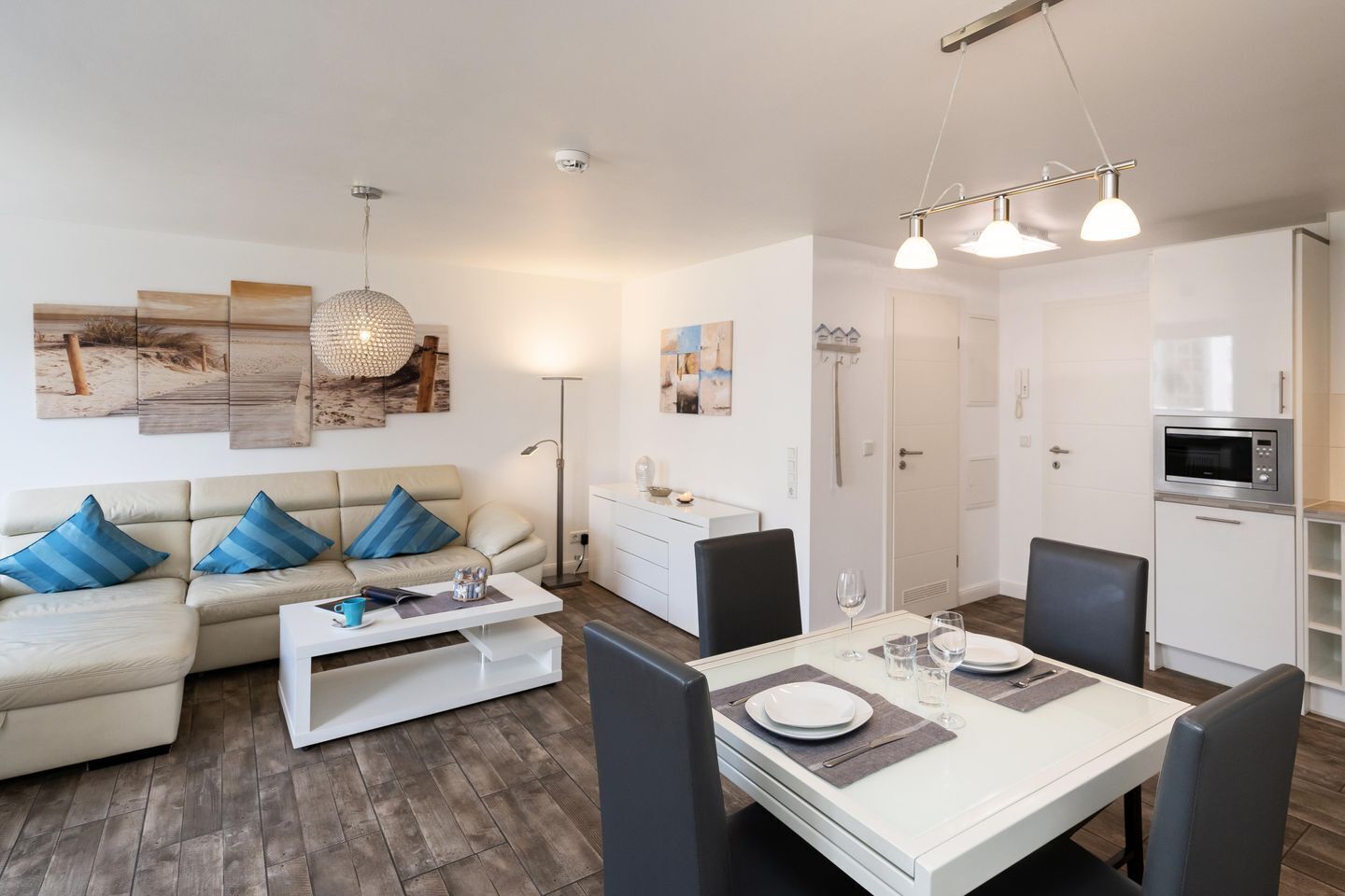 A modern living room with a sofa, coffee table, and dining table set for two. There is a kitchen area with a microwave and cabinets.