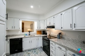 A modern kitchen with white cabinetry, a black dishwasher, and a granite countertop. - Cottage in Richmond Hill, Pet Friendly with King Bed (Richmond Hill)