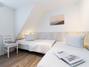 A bedroom with two single beds, a small white chair, and a wall-mounted painting.