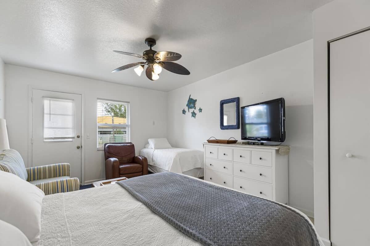 A bedroom with a bed, a chair, a dresser, a television, and a ceiling fan.