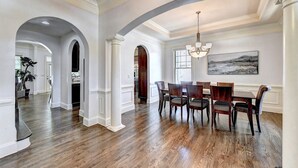 Una spaziosa sala da pranzo con soffitto alto, pavimento in legno e lampadario.