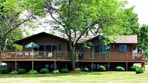 A two-story house with a deck and a covered patio area. - Exclusive Lakefront Home Retreat w/Baby Grand Piano for Family FLX Fun & Friends (Ovid)
