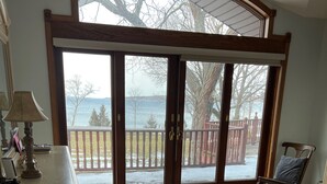 A spacious room with a large sliding glass door leading to a balcony with a view of the sea. - Exclusive Lakefront Home Retreat w/Baby Grand Piano for Family FLX Fun & Friends (Ovid)