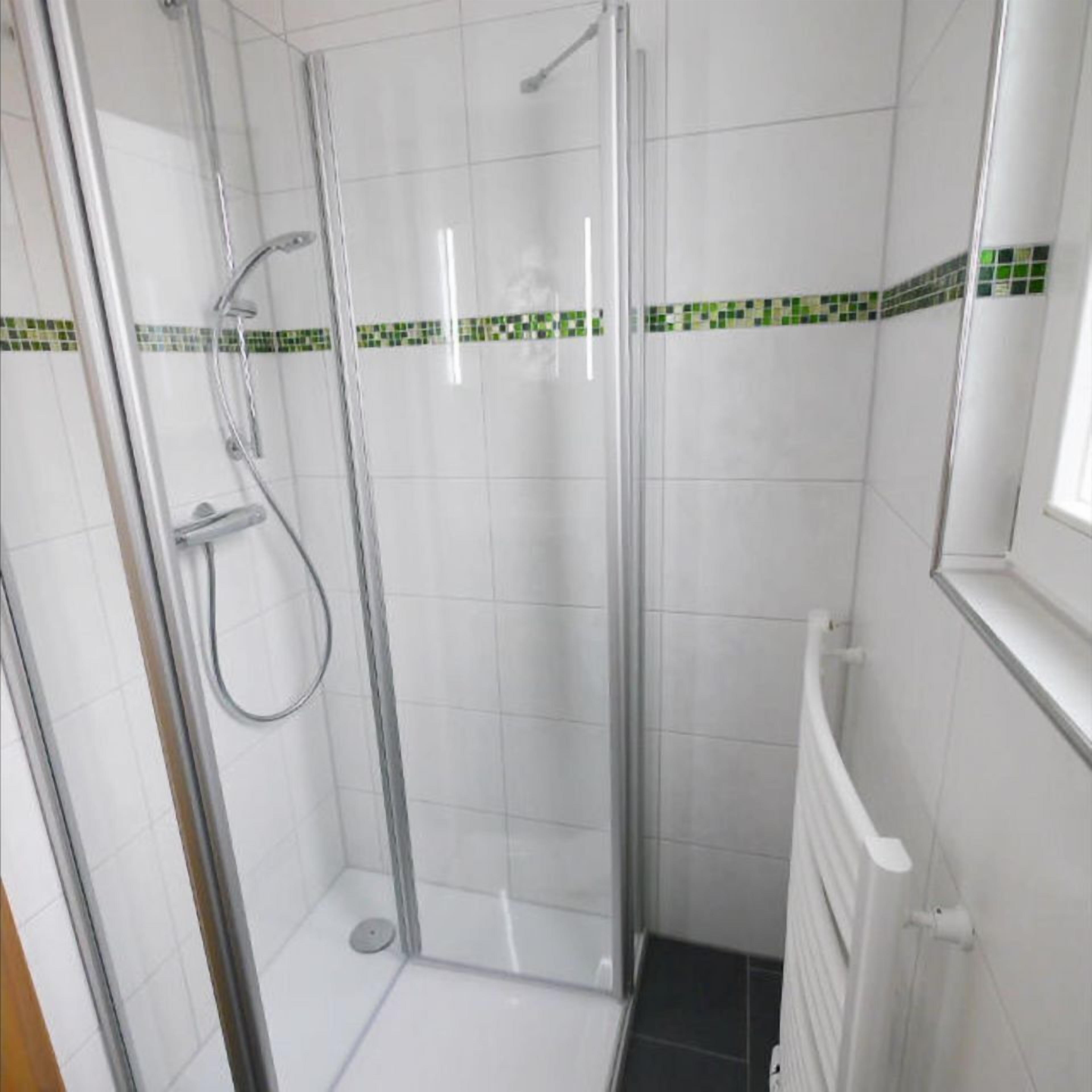 Un box de ducha con paredes de vidrio, suelo de azulejos y un borde verde y blanco.