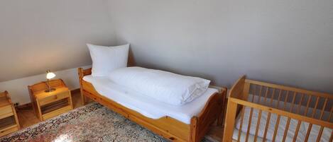 Een kleine, verzorgde slaapkamer met een enkel bed, een houten ledikant, een nachtkastje met een lamp en een kamerkleed met een patroon.