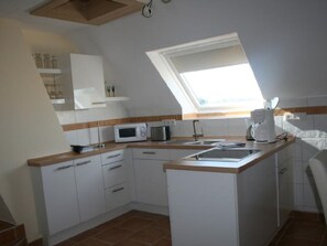 Cocina compacta con armarios blancos, microondas, cafetera y ventana.