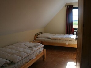 Un dormitorio con dos camas individuales, cabecero de madera, ventana con cortinas y suelo de baldosas.