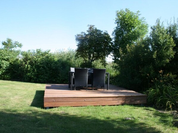 Un área de patio exterior con cubierta de madera, dos sillas y una mesa.