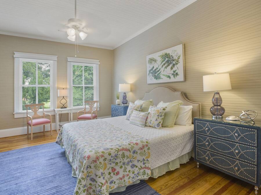 A bedroom with a bed, two windows, a chair, a dresser, and a ceiling fan.