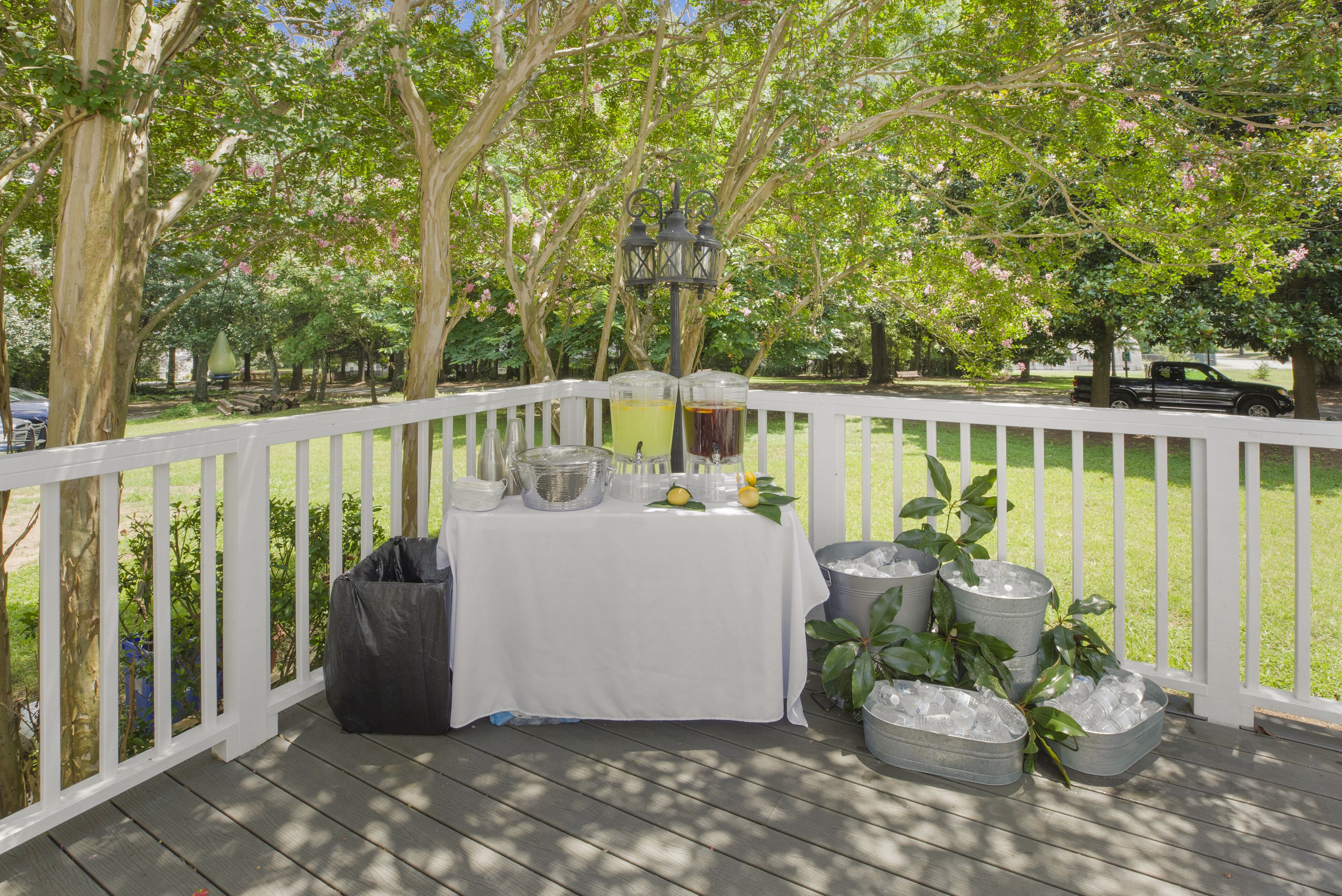 A covered outdoor area with a table set up for a gathering, surrounded by trees and a white fence.