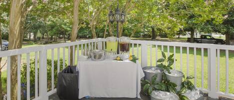 A covered outdoor area with a table set up for a gathering, surrounded by trees and a white fence.