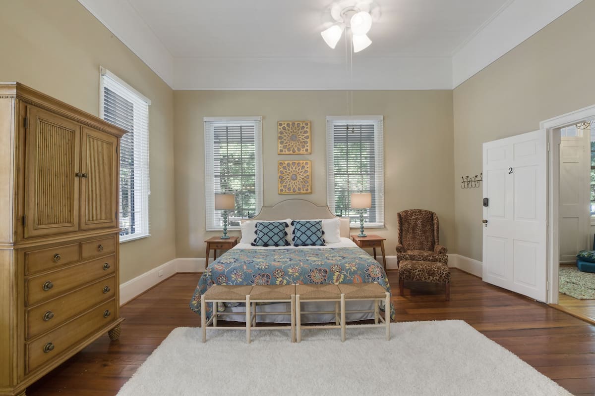 A bedroom with a large bed, a wardrobe, two bedside tables, a chair, and a door.