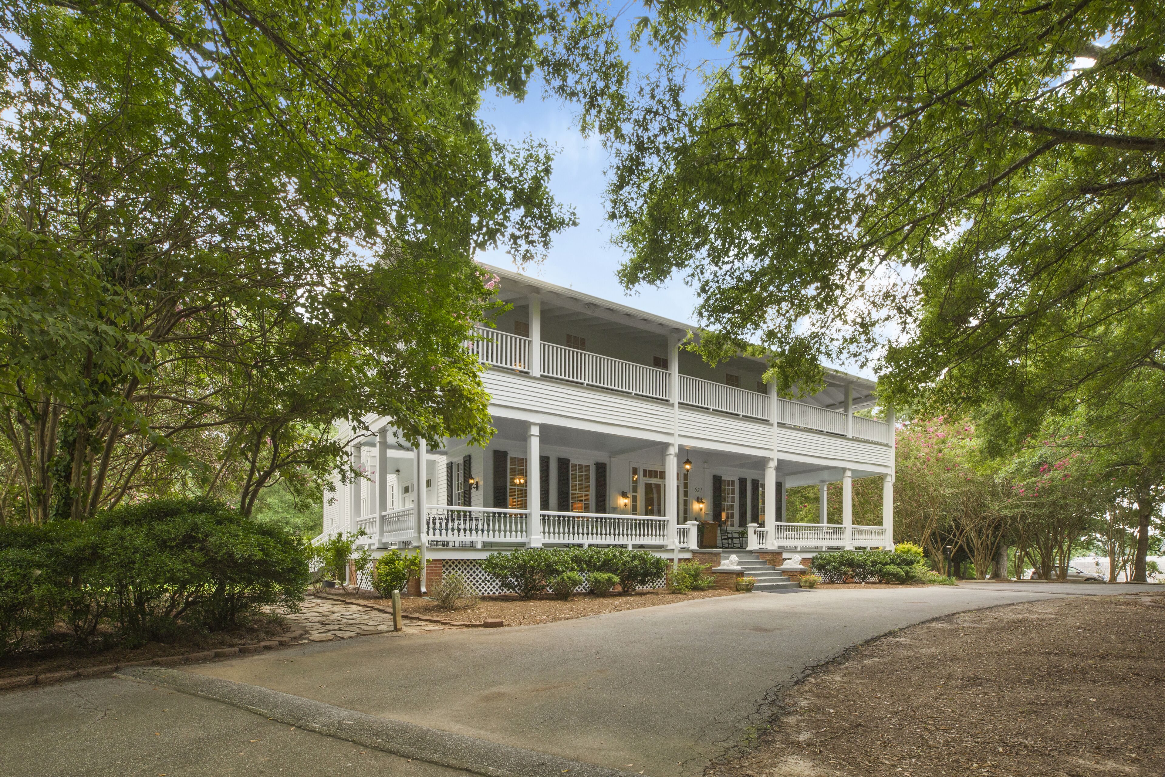 A two-story white building with a balcony, surrounded by trees and a paved driveway.